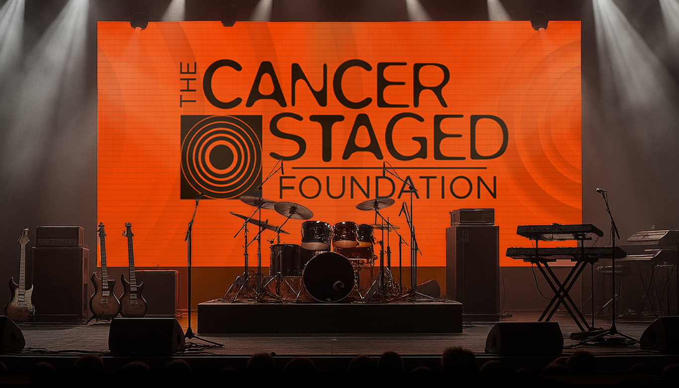 Concert stage with The Cancer Staged Foundation logo displayed on a large screen, surrounded by instruments and stage lighting